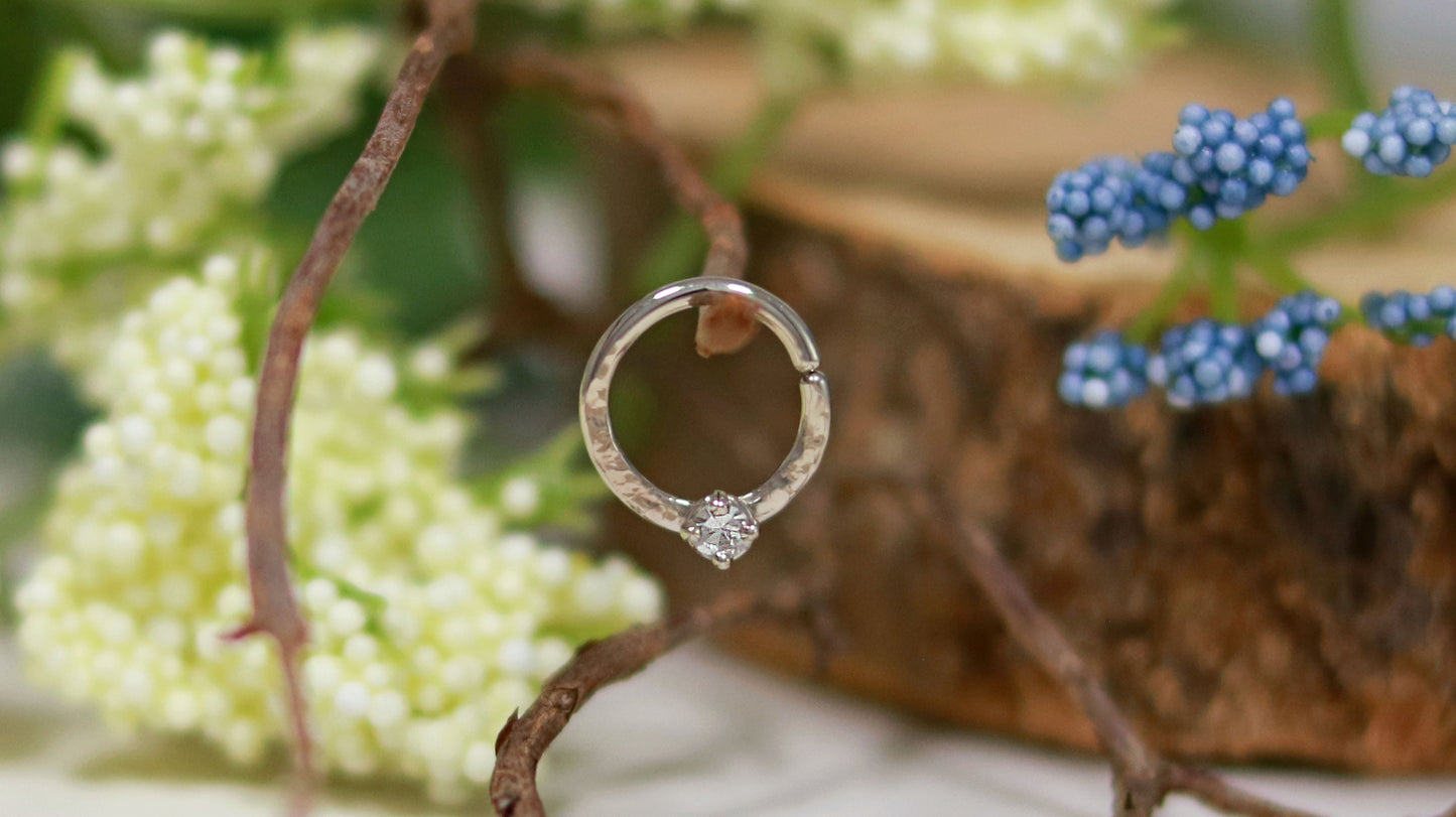 A 14k white gold hoop, flattened and textured at the bottom, with a round diamond set with prongs on top of the textured flat section.
