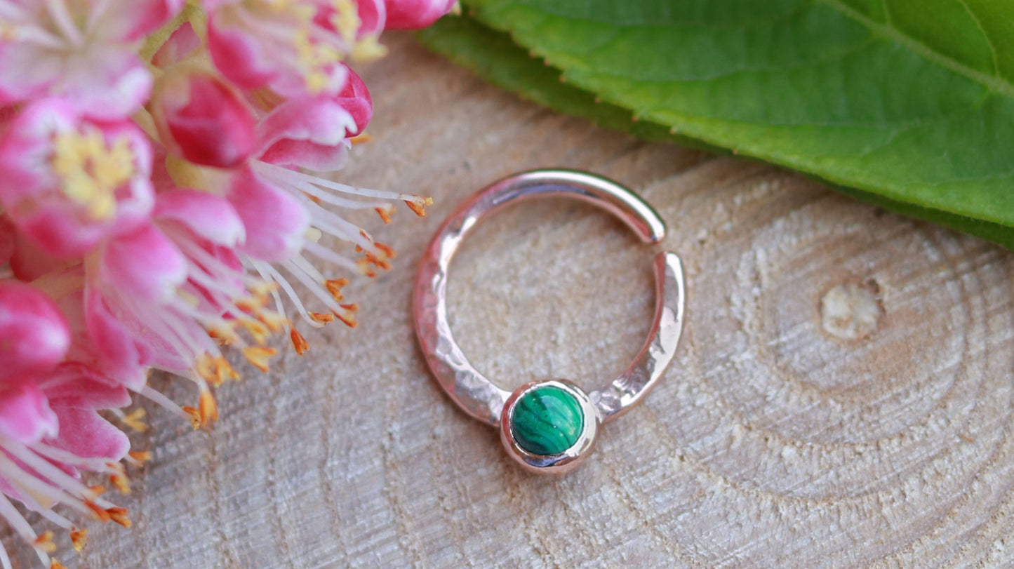 A 14k rose gold hoop, flattened and textured at the bottom, with a round malachite set in a bezel on top of the textured flat section.