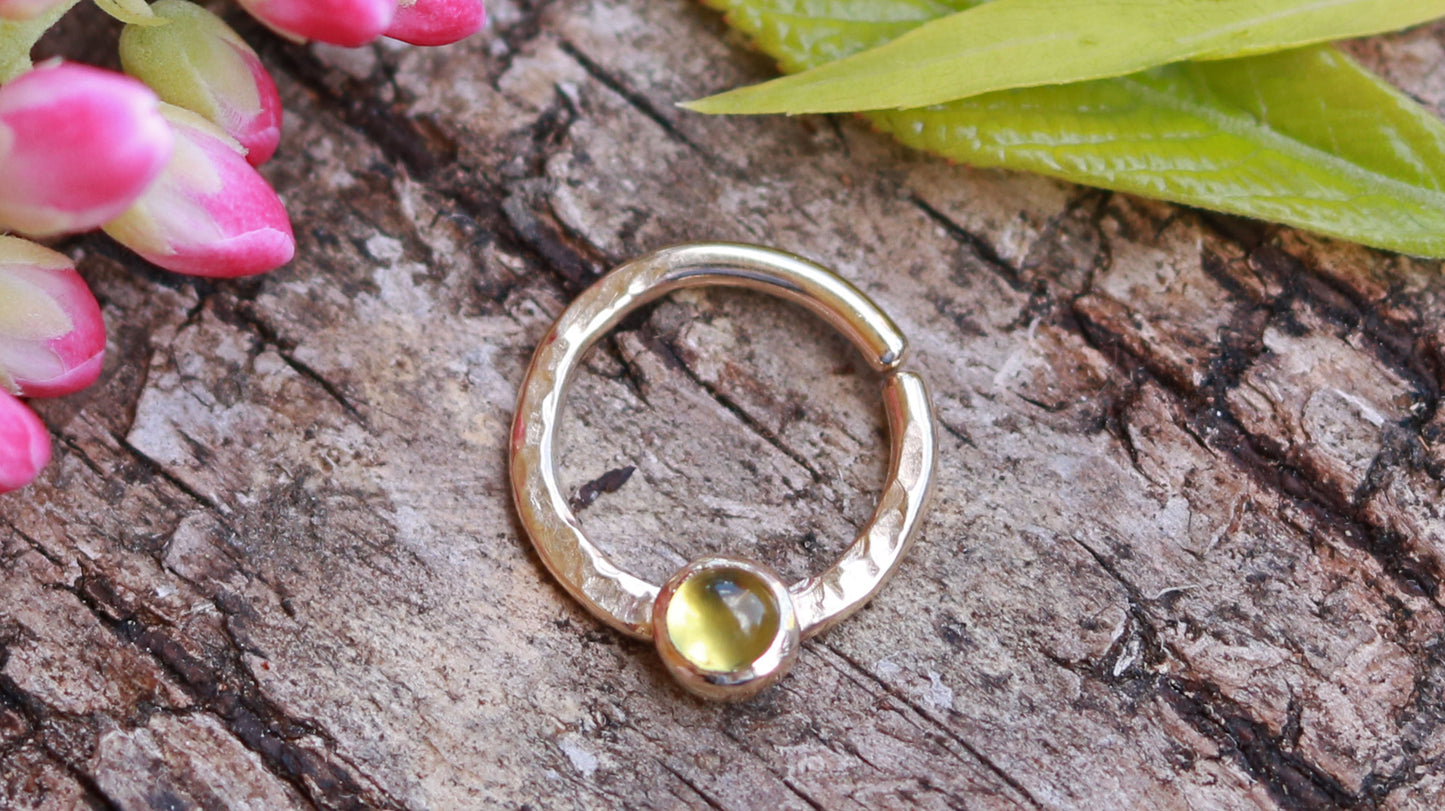 A 14k yellow gold hoop, flattened and textured at the bottom, with a round peridot set in a bezel on top of the textured flat section.