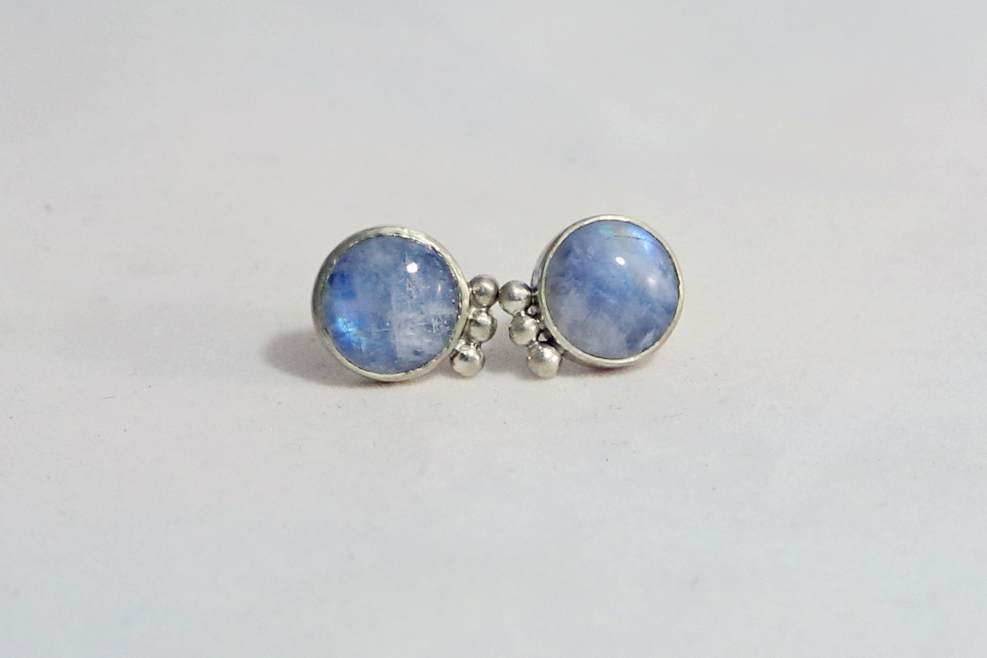 A pair of round rainbow moonstone stud earrings with 3 silver bubbles in a row on the sides.