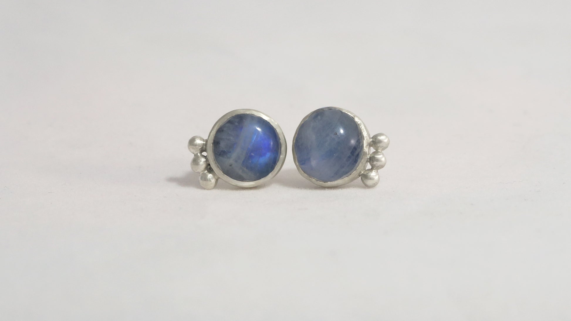 A pair of round rainbow moonstone stud earrings with 3 silver bubbles in a row on the sides..