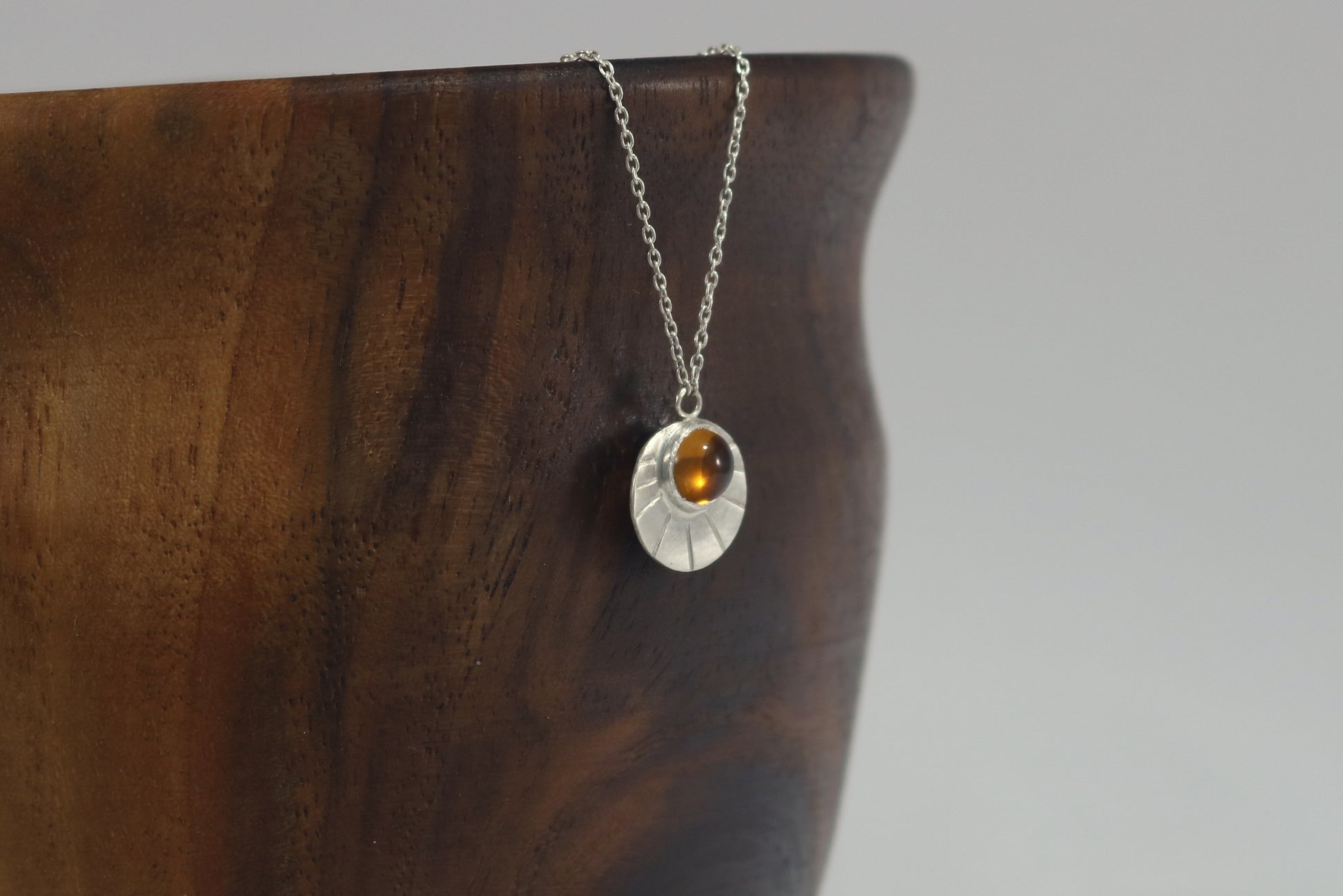 Sterling silver disc with natural gemstone set in bezel at the top with black lines bursting from it on a sterling silver chain.