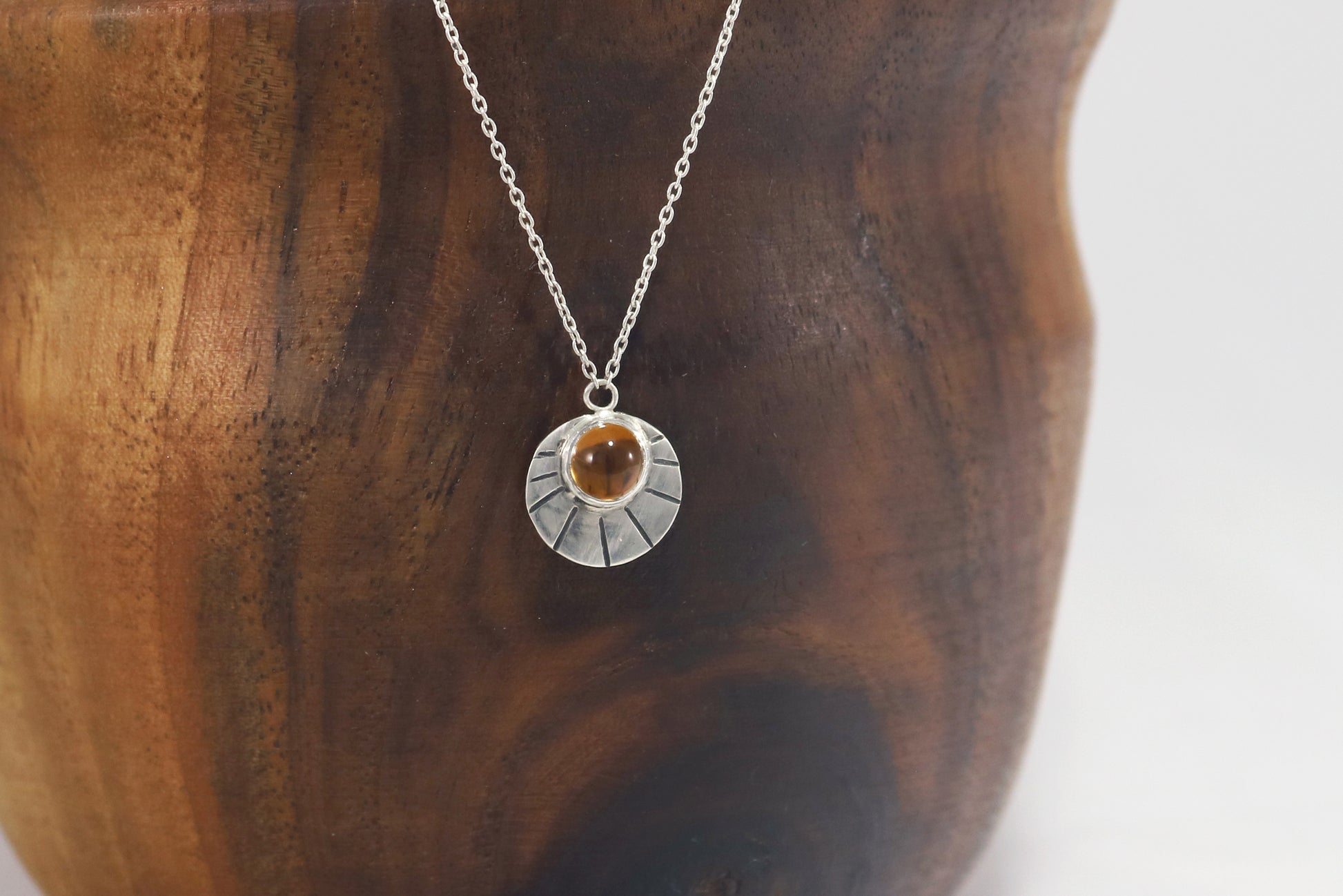 Sterling silver disc with natural gemstone set in bezel at the top with black lines bursting from it on a sterling silver chain.