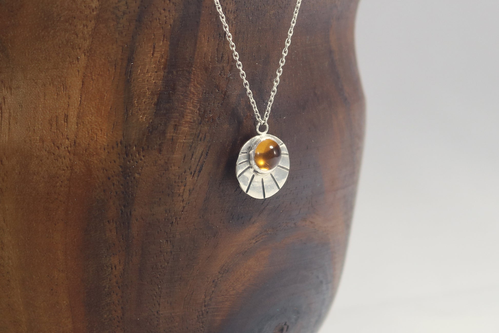 Sterling silver disc with natural gemstone set in bezel at the top with black lines bursting from it on a sterling silver chain.