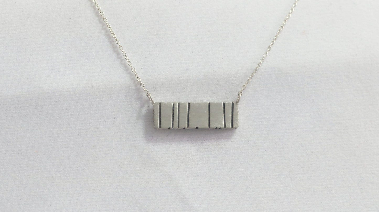 A large sterling silver bar with randomly spaced black lines.