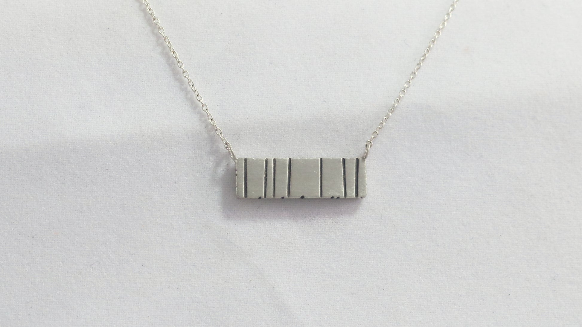 A large sterling silver bar with randomly spaced black lines.