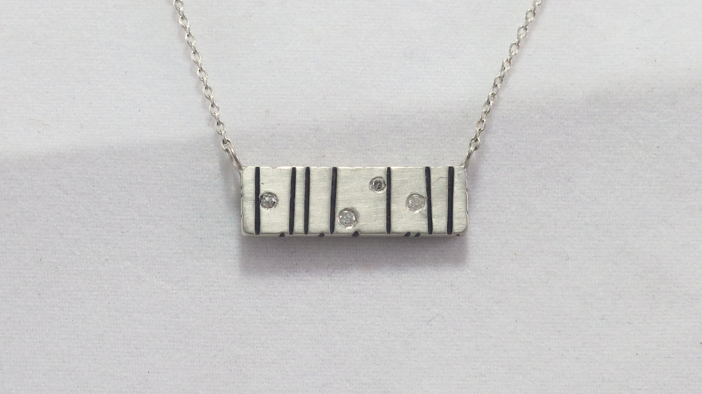 A large sterling silver bar with randomly spaced black lines and 4 white flush set diamonds.