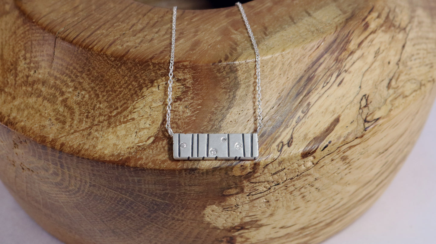 A large sterling silver bar with randomly spaced black lines and 4 white flush set diamonds.