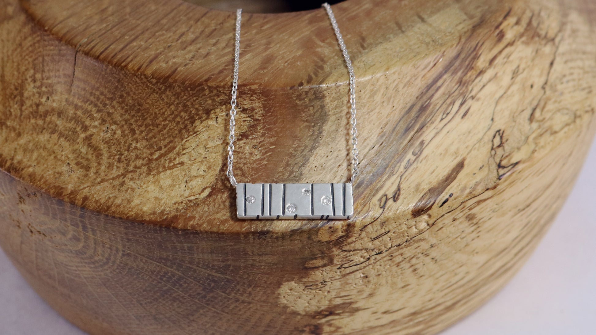 A large sterling silver bar with randomly spaced black lines and 4 white flush set diamonds.