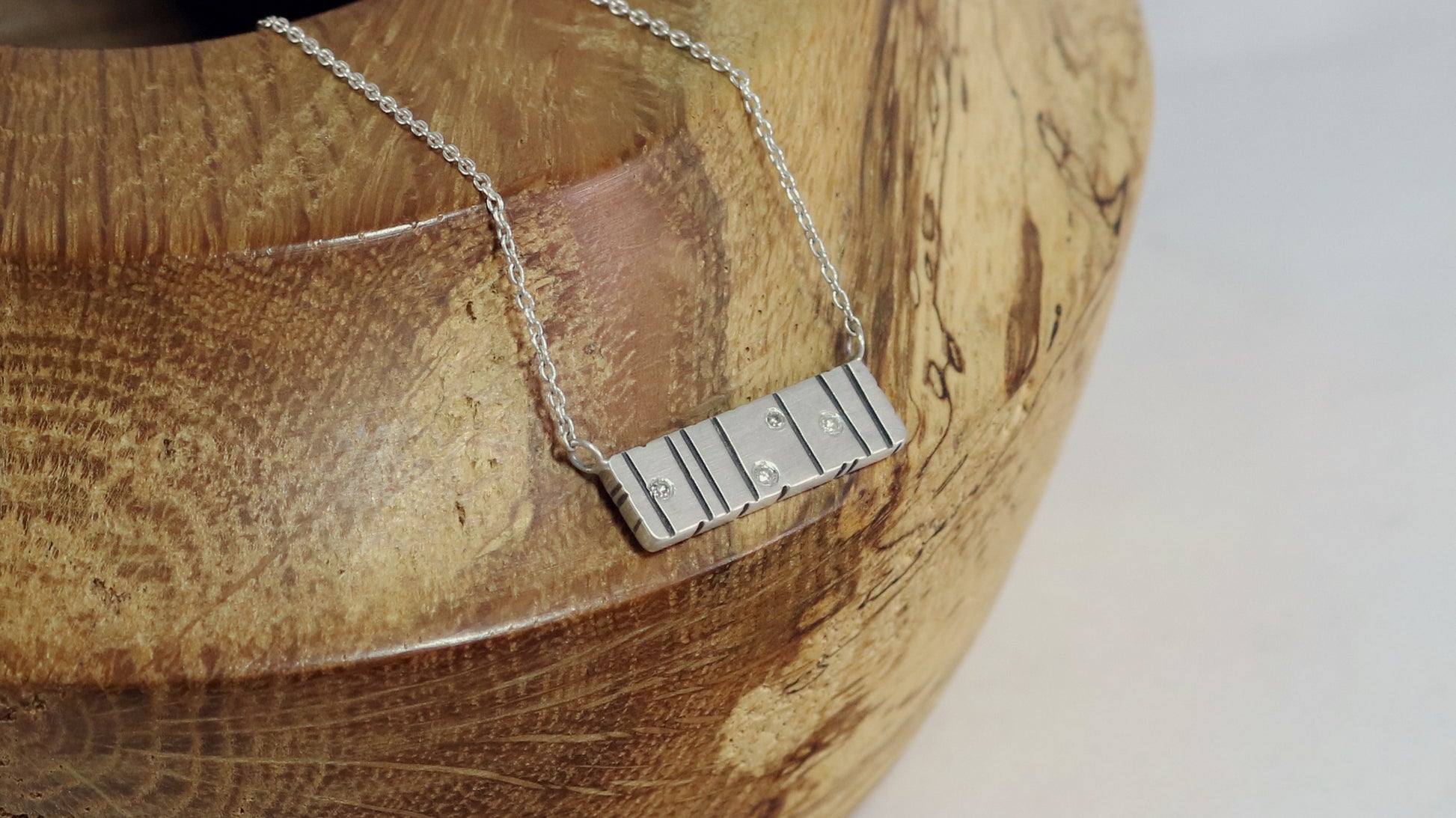 A large sterling silver bar with randomly spaced black lines and 4 white flush set diamonds.