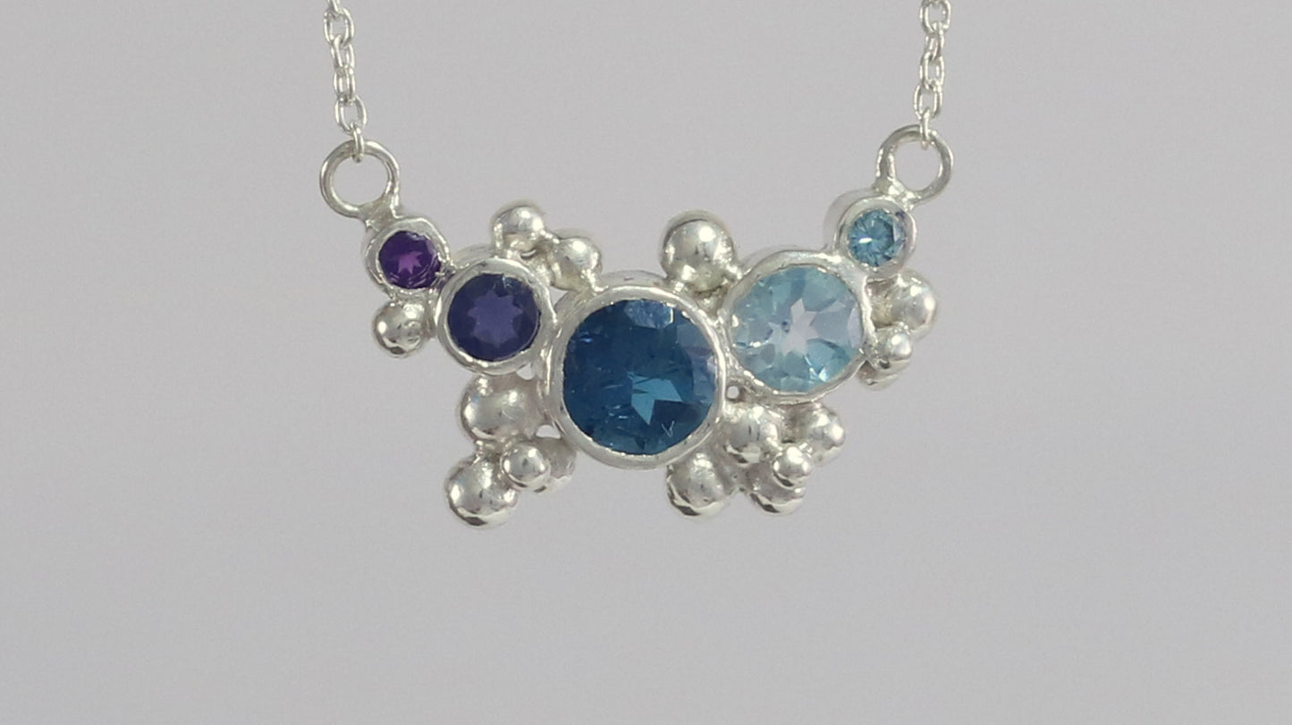 Different shades of natural round blue gemstones, surrounded by silver bubbles on a silver chain.