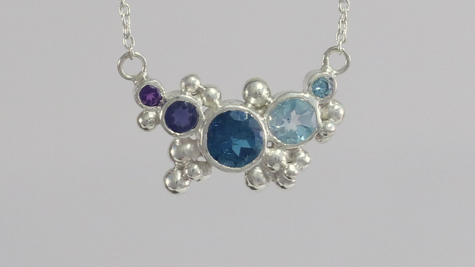 Different shades of natural round blue gemstones, surrounded by silver bubbles on a silver chain.