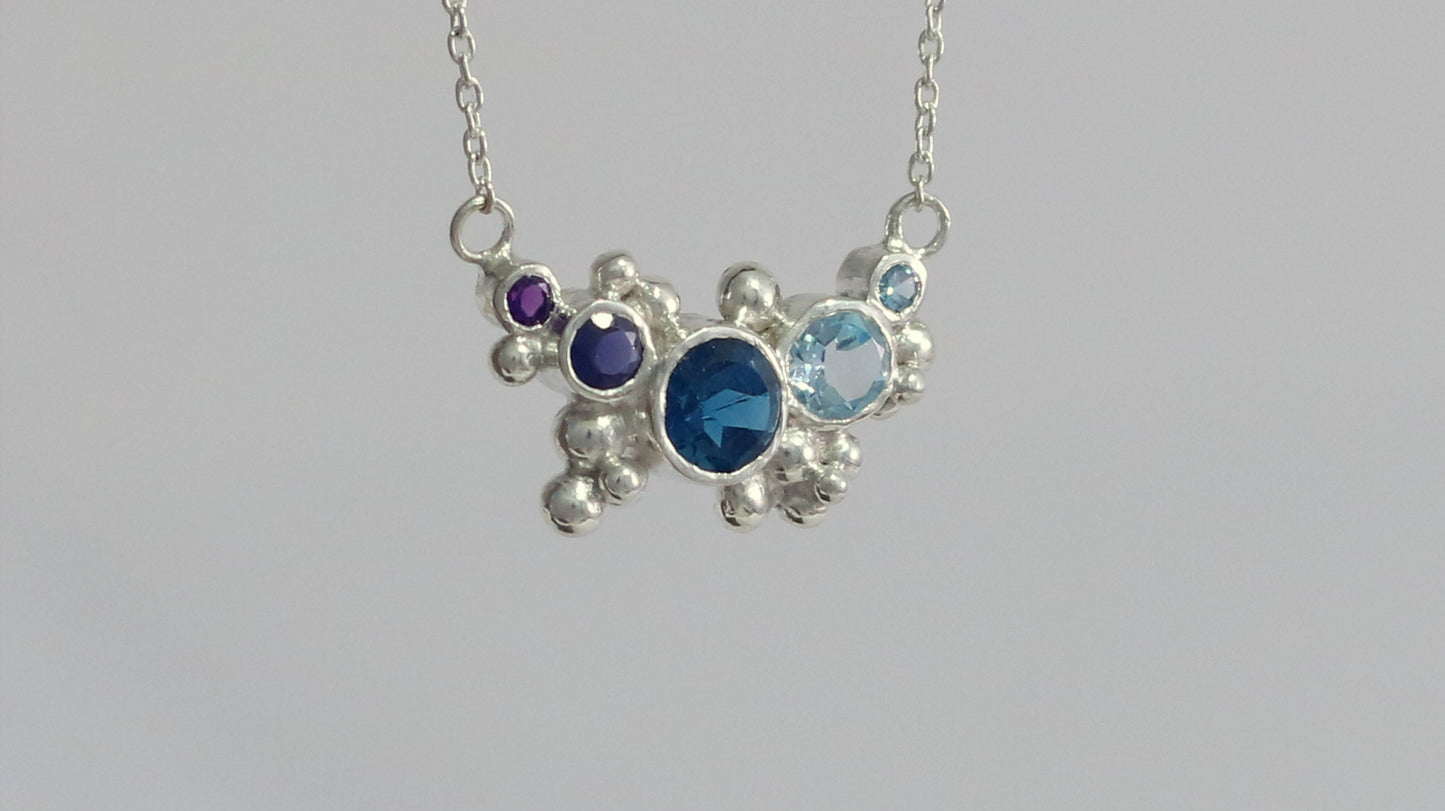 Different shades of natural round blue gemstones, surrounded by silver bubbles on a silver chain.