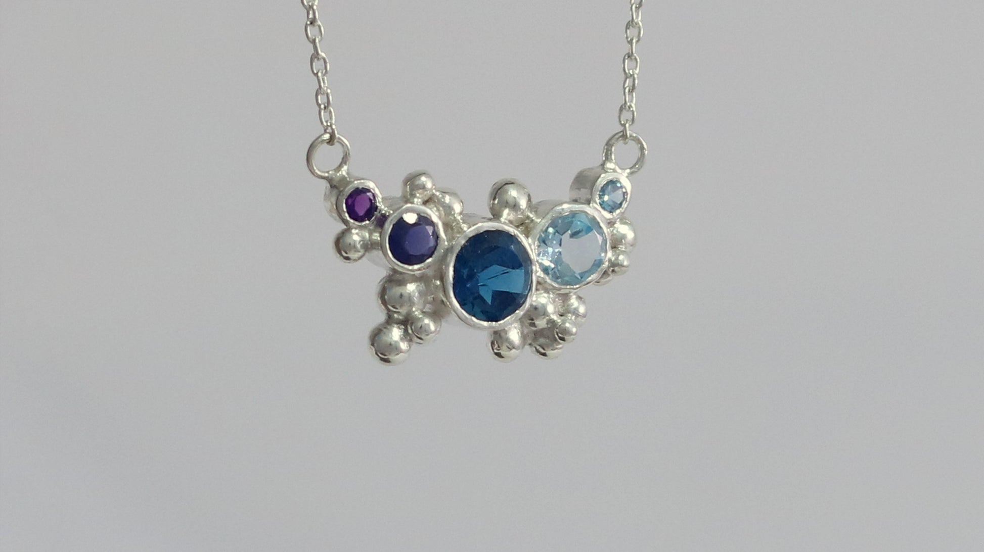 Different shades of natural round blue gemstones, surrounded by silver bubbles on a silver chain.