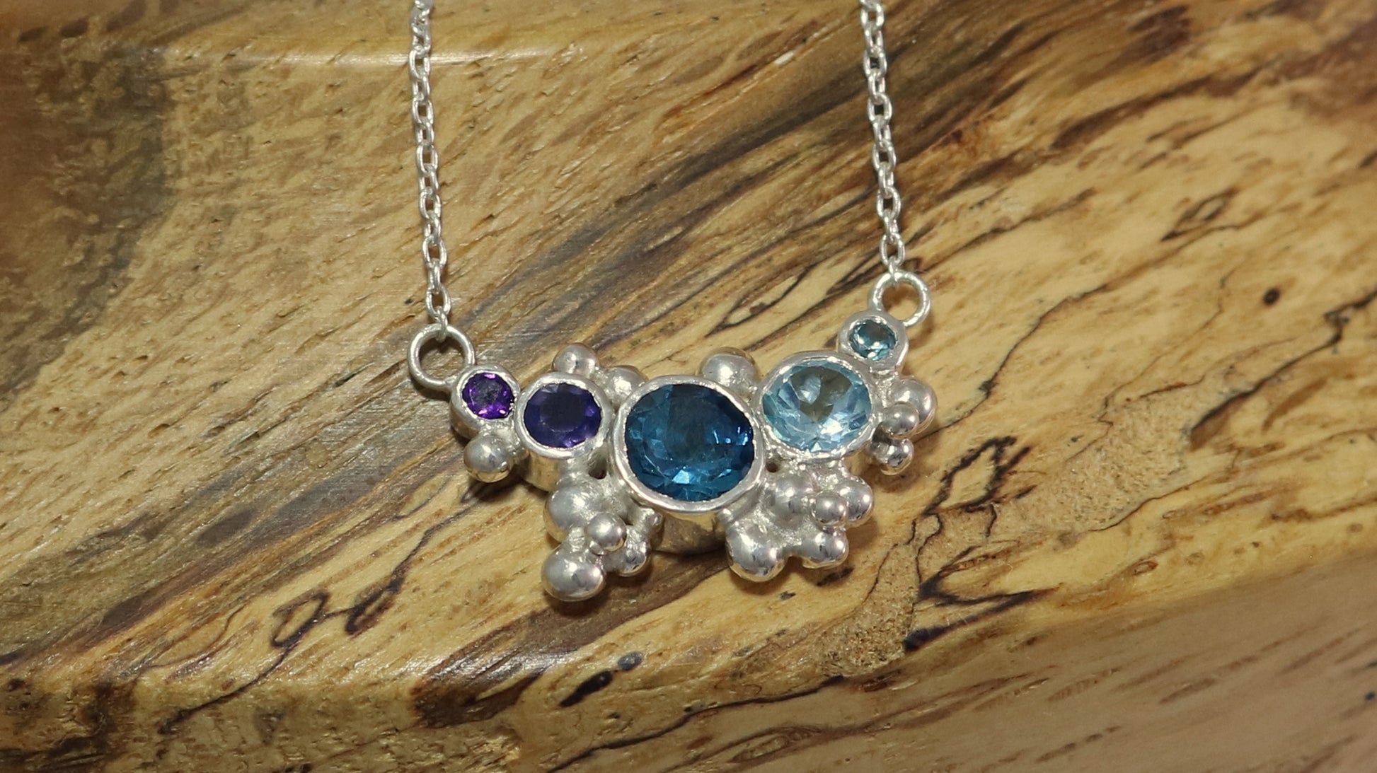 Different shades of natural round blue gemstones, surrounded by silver bubbles on a silver chain.