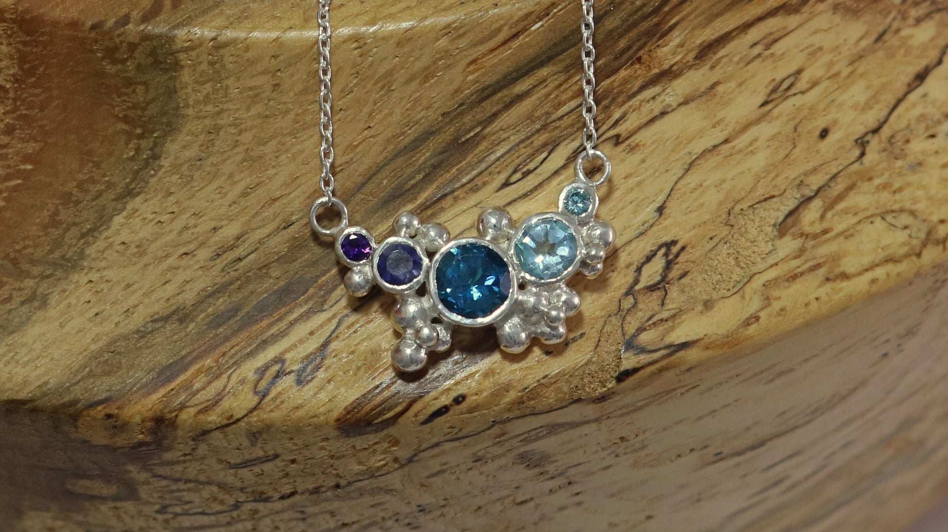 Different shades of natural round blue gemstones, surrounded by silver bubbles on a silver chain.