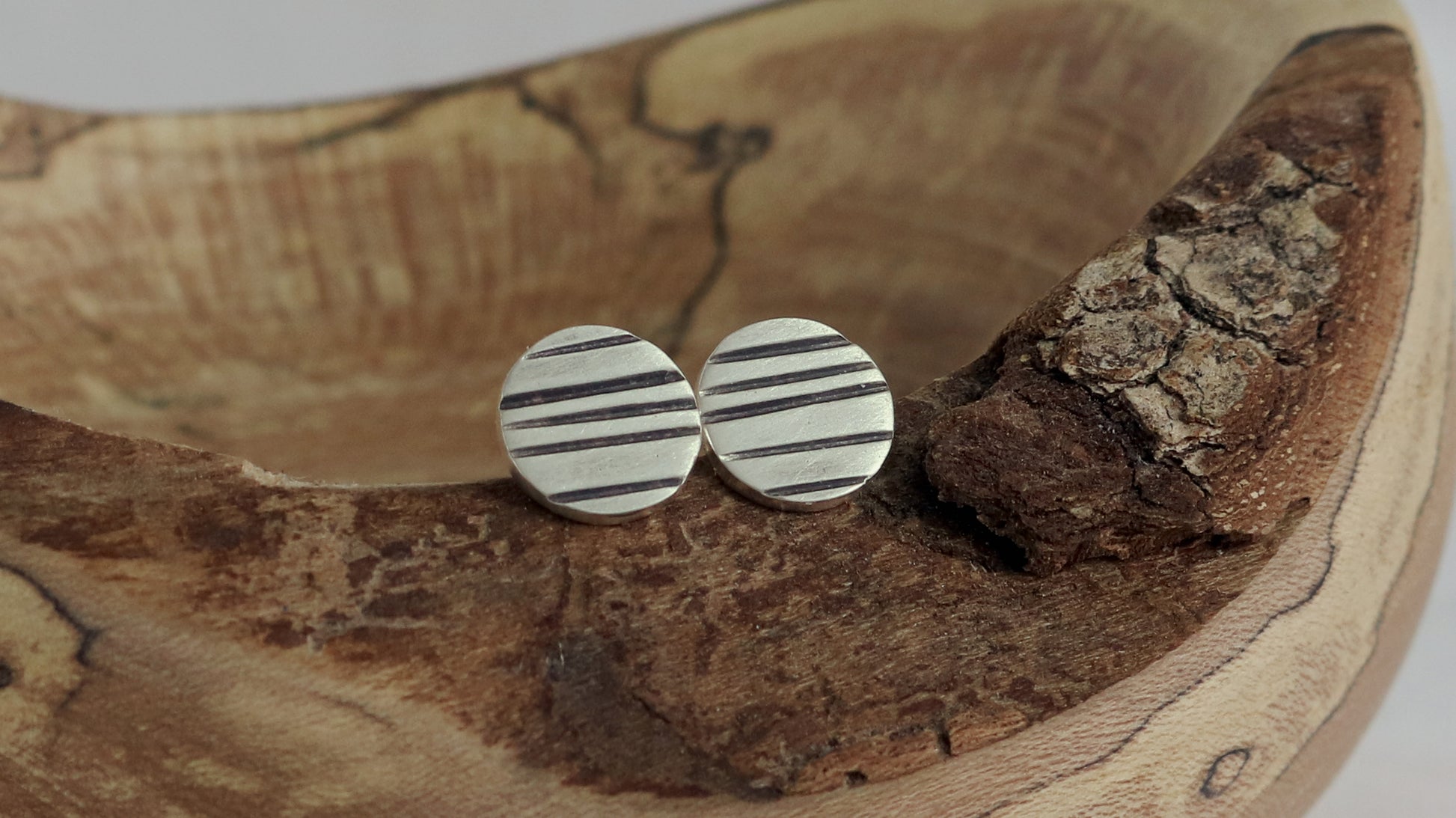 Round silver disc studs with black lines randomly spaced.