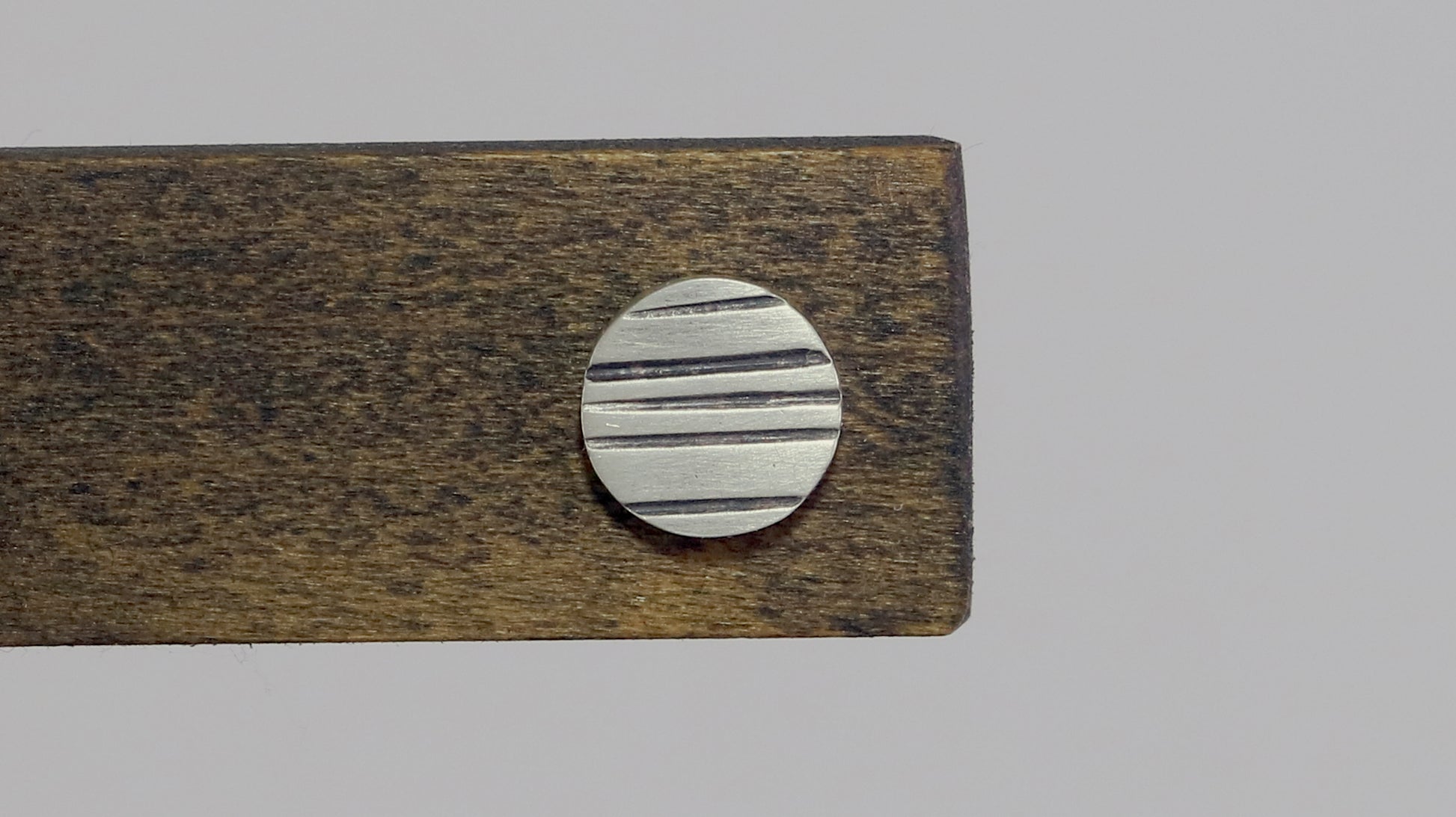 Round silver disc studs with black lines randomly spaced.