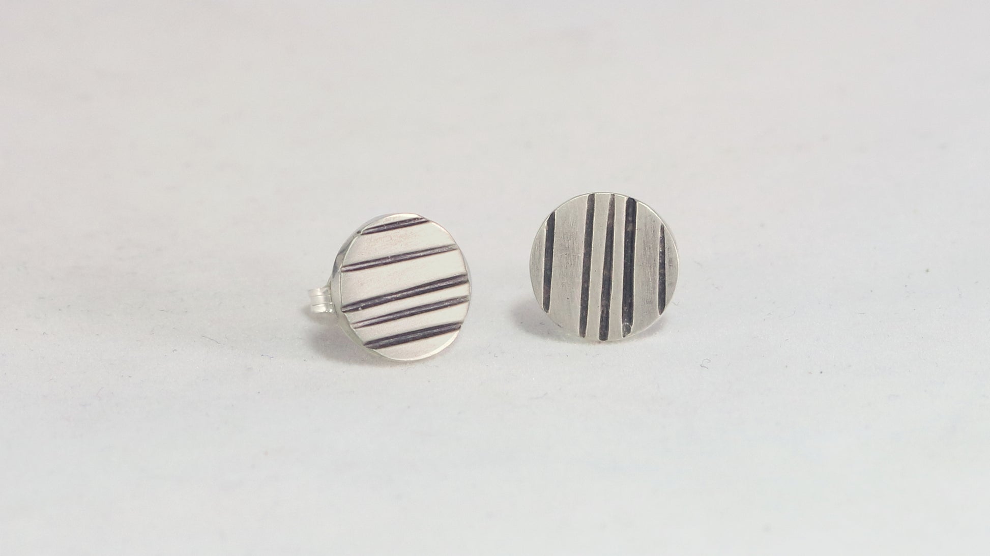 Round silver disc studs with black lines randomly spaced.