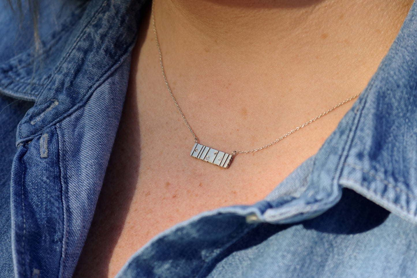 A large sterling silver bar with randomly spaced black lines and 4 white flush set diamonds.