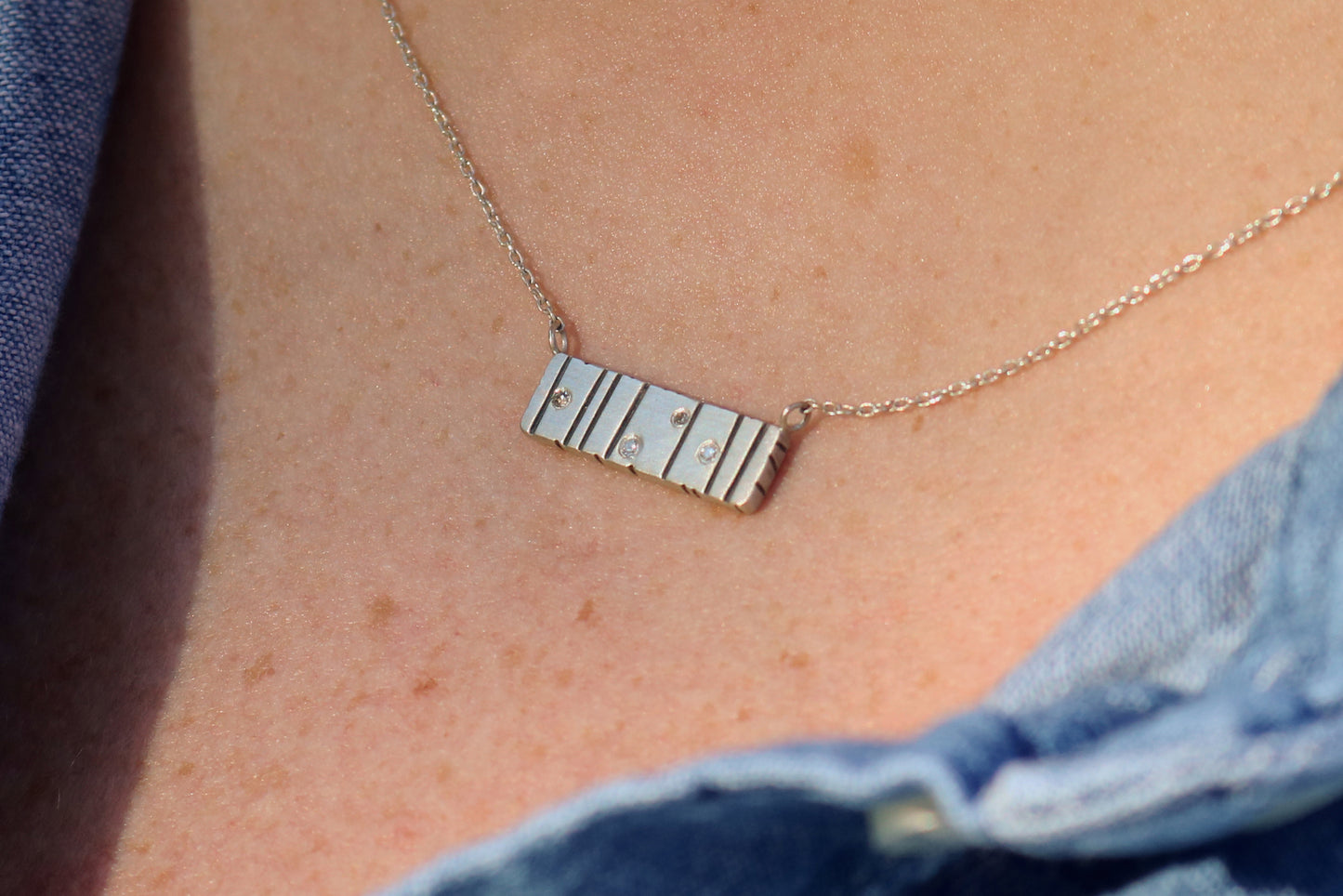 A large sterling silver bar with randomly spaced black lines and 4 white flush set diamonds.