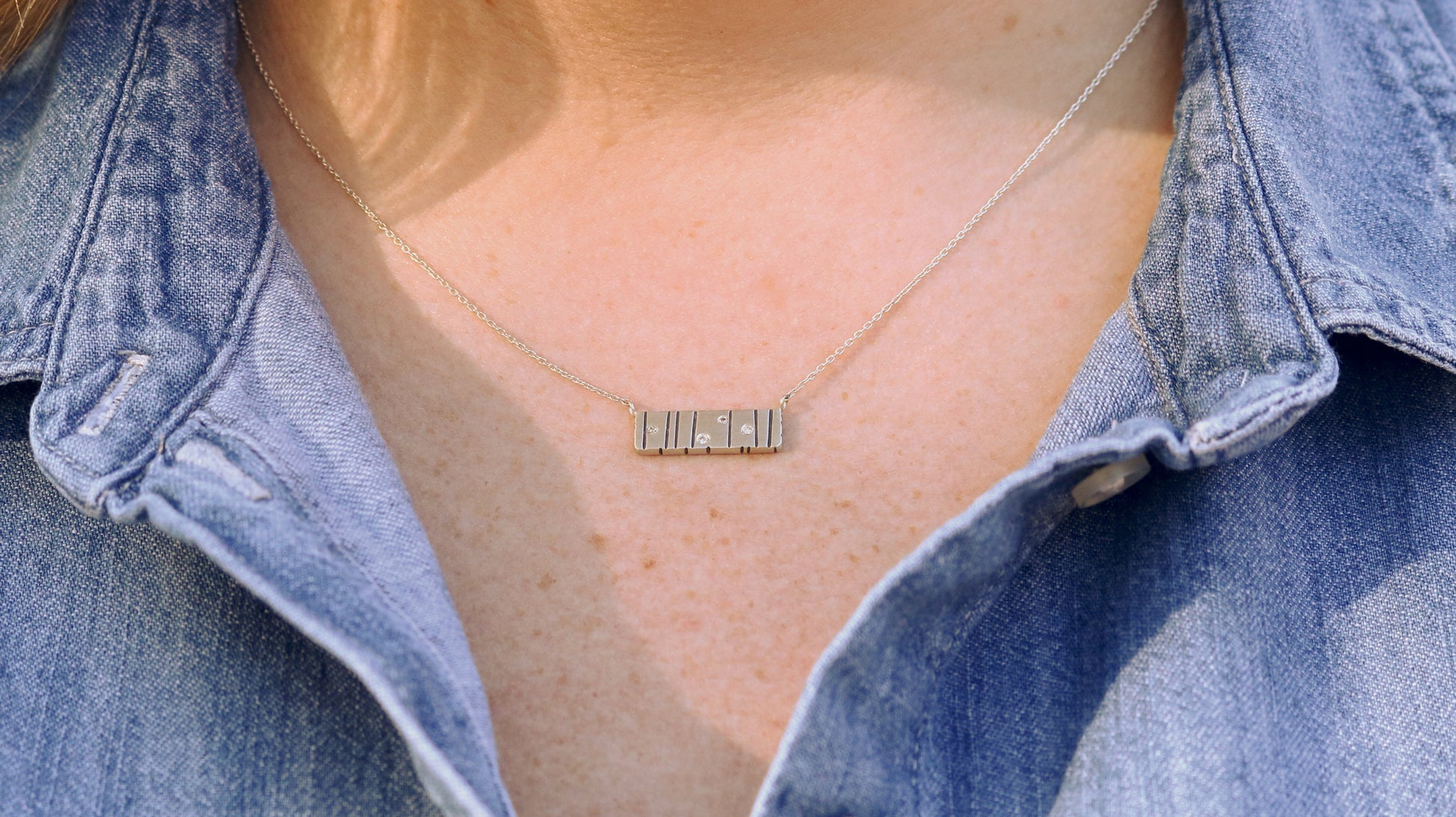 A large sterling silver bar with randomly spaced black lines and 4 white flush set diamonds.