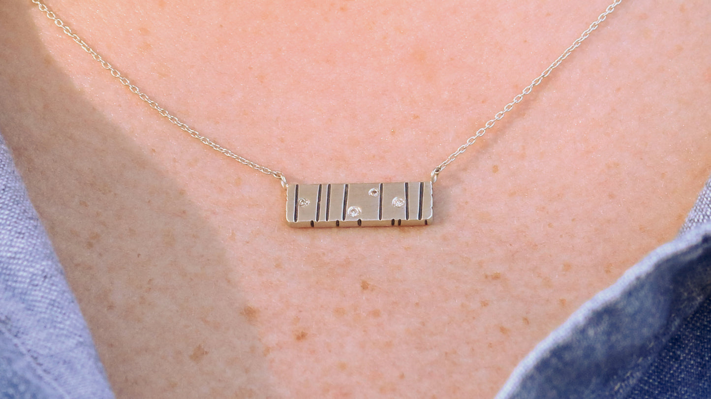 A large sterling silver bar with randomly spaced black lines and 4 white flush set diamonds.