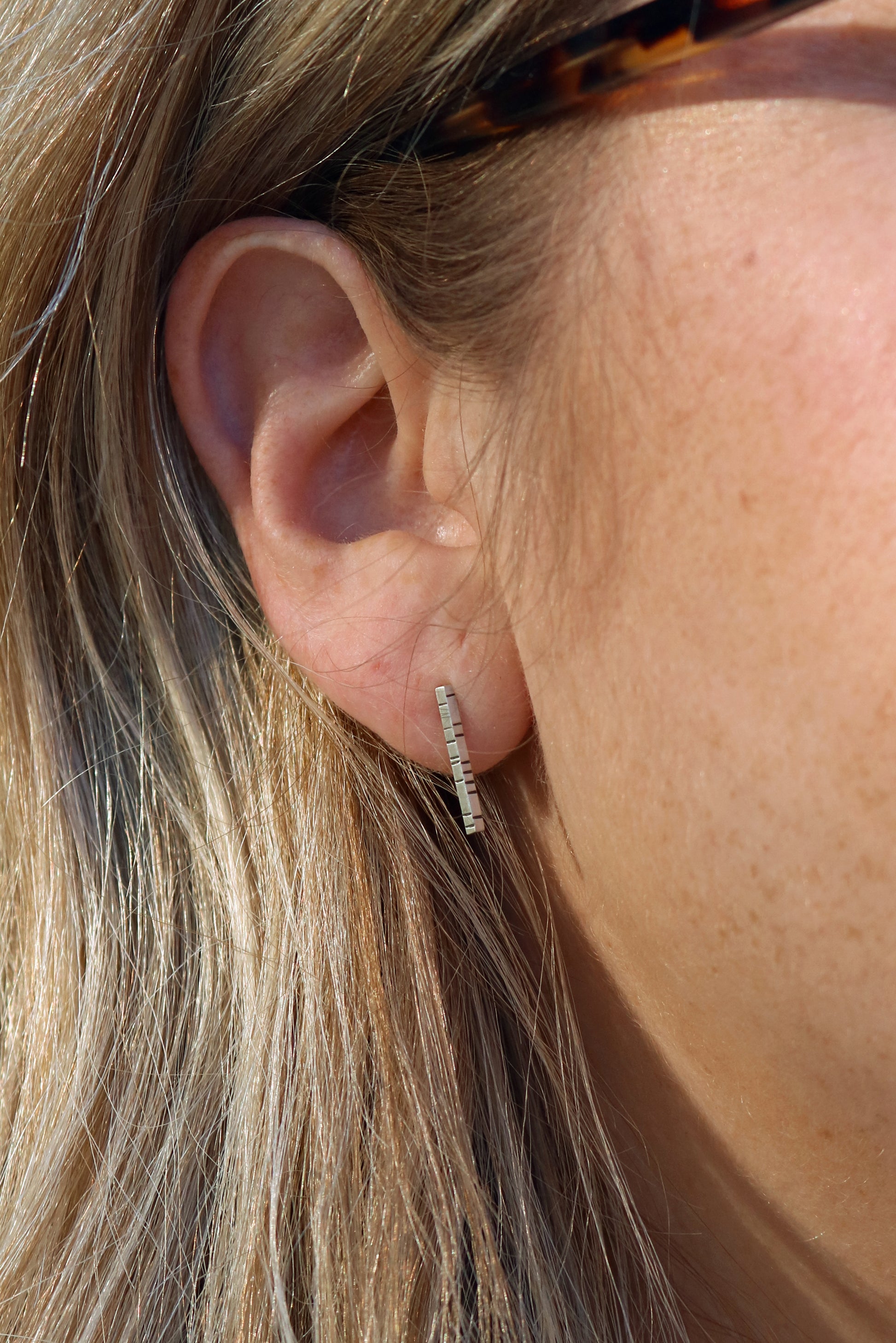 A model wearing 1.5mm thick solid sterling silver, rectangle bar studs with randomly spaced black lines.