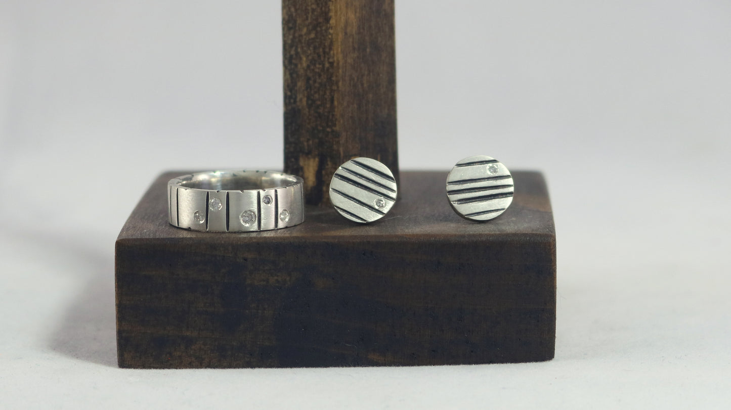 Round silver disc studs with black lines randomly spaced and a single white diamond flush set at the edge.