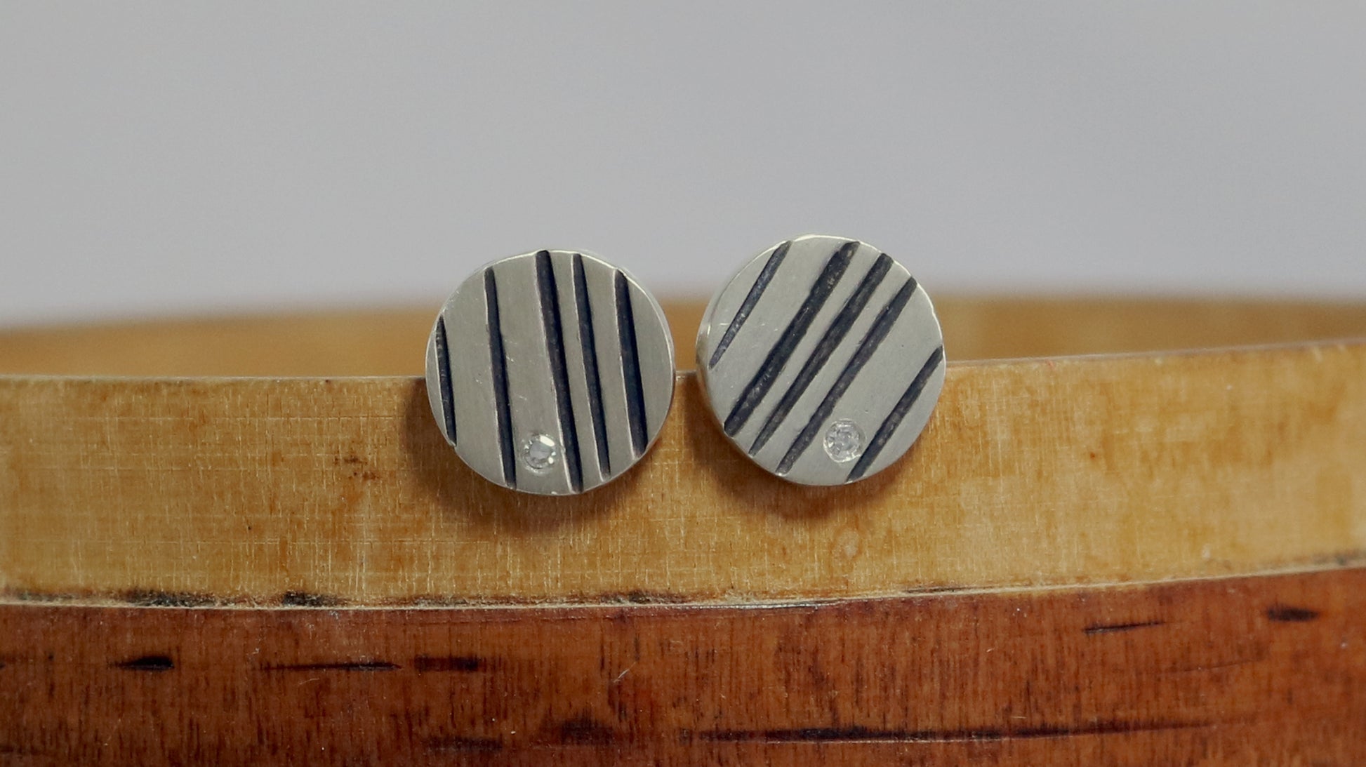 Round silver disc studs with black lines randomly spaced and a single white diamond flush set at the edge.