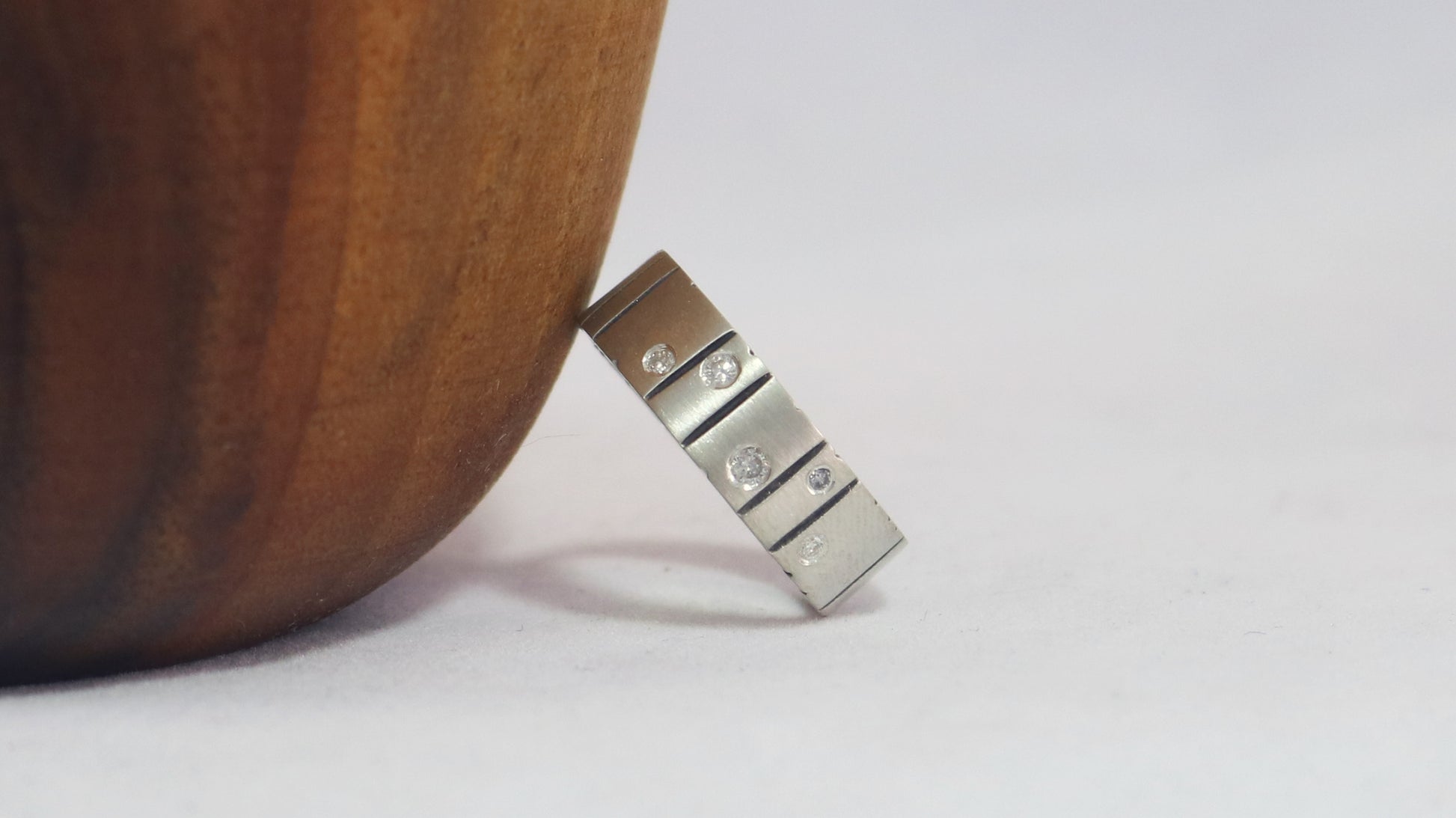 A thick silver ring band with randomly spaced black line details is flush set with 5 various sized diamonds.