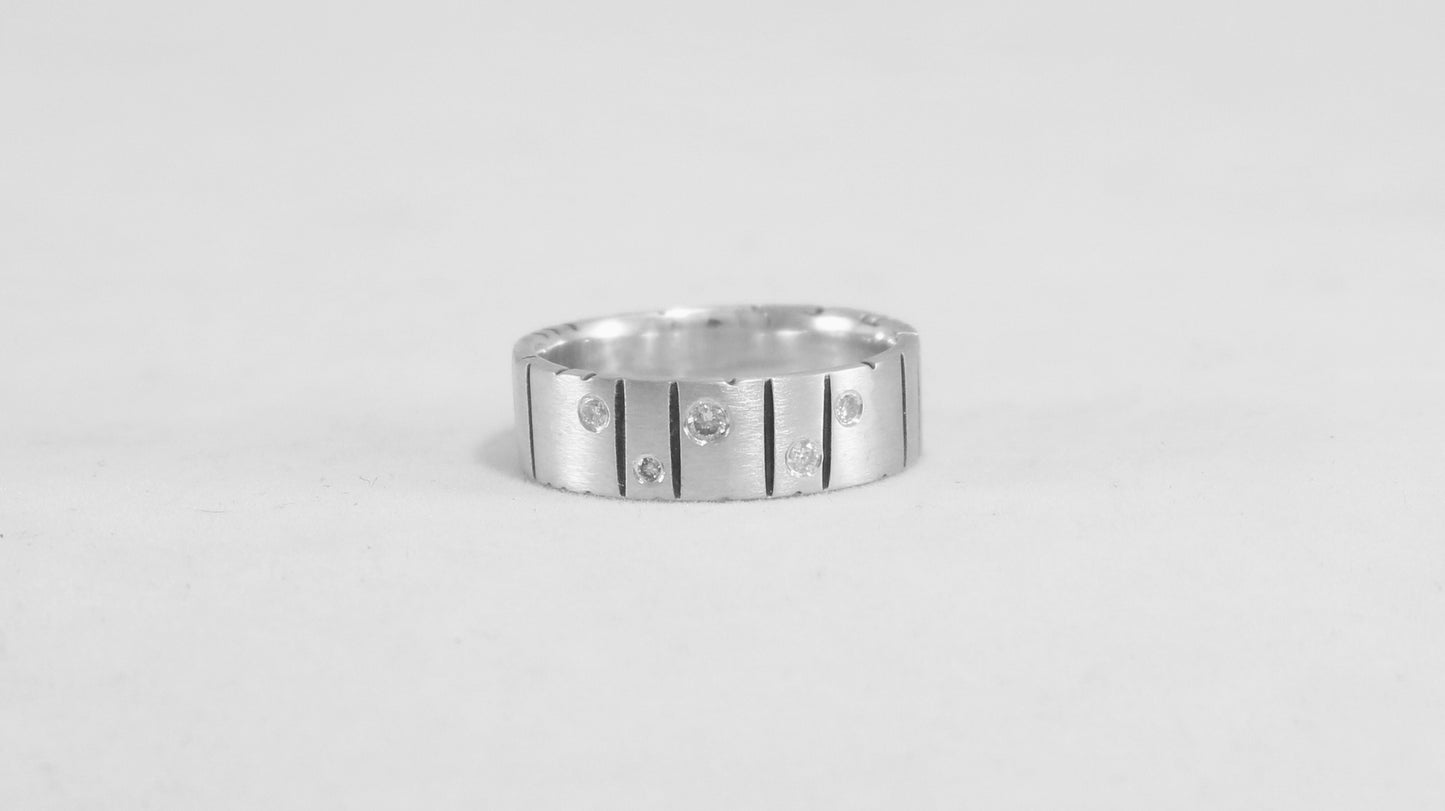 A thick silver ring band with randomly spaced black line details is flush set with 5 various sized diamonds.