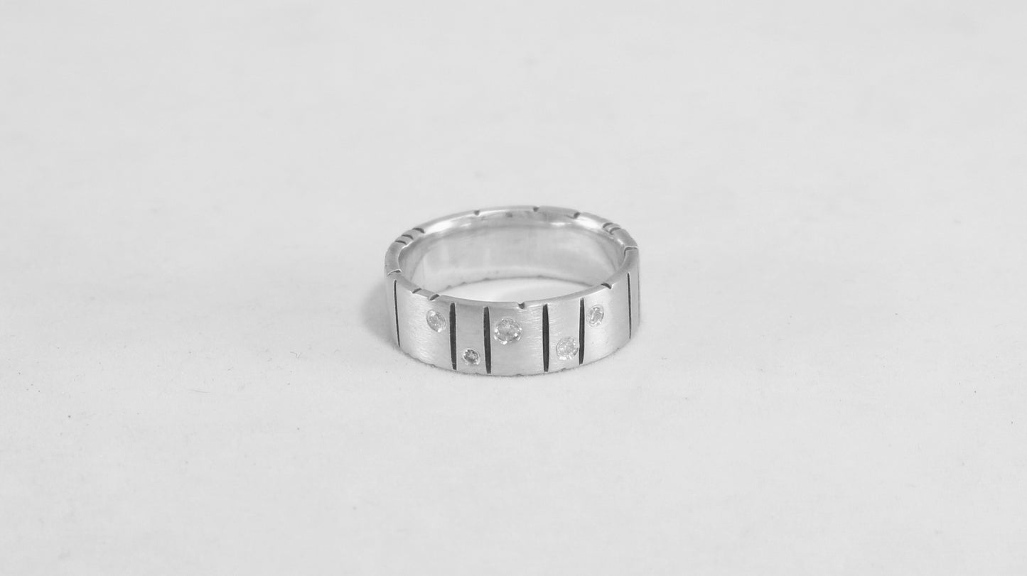 A thick silver ring band with randomly spaced black line details is flush set with 5 various sized diamonds.