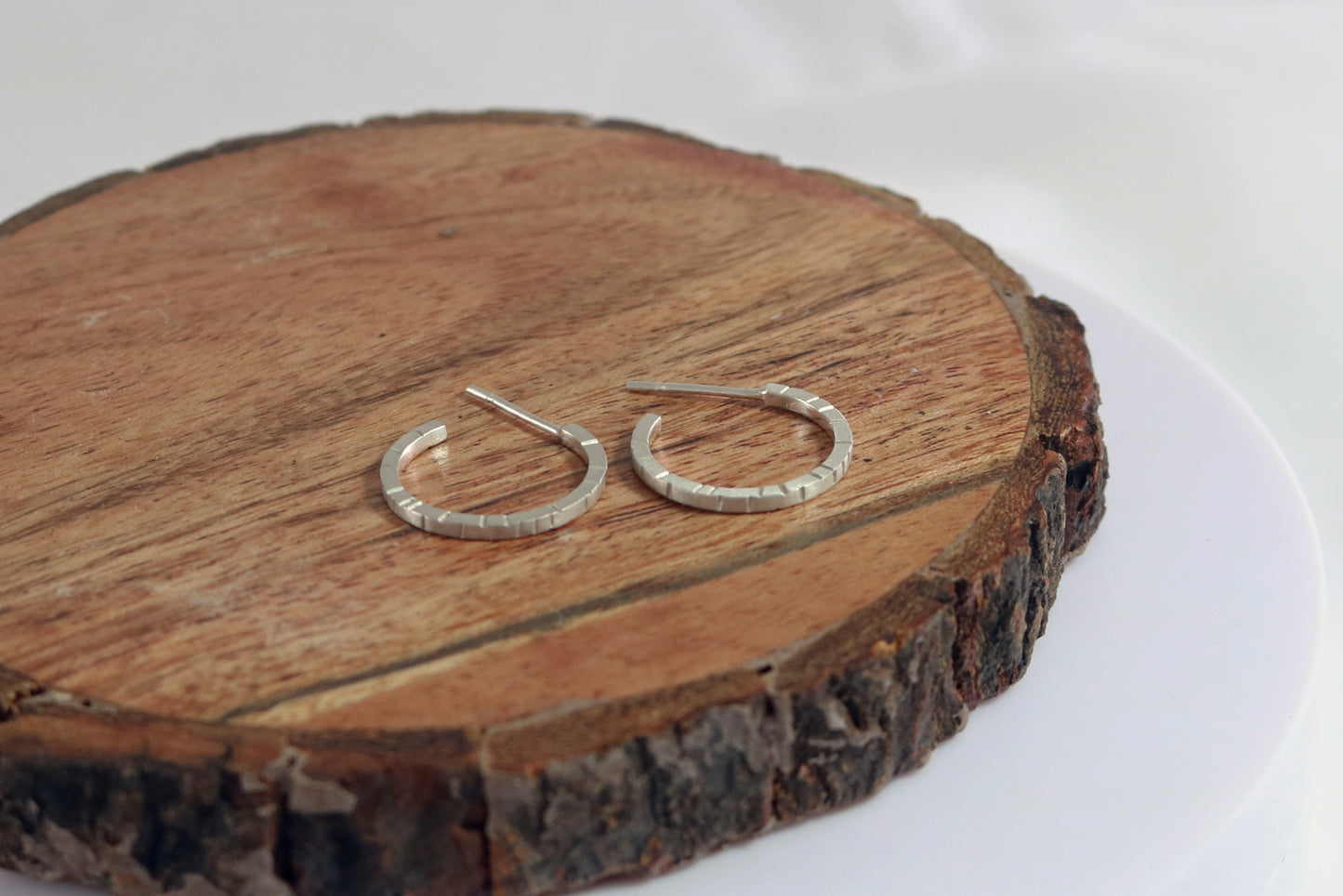 Thin sterling silver hoop earrings with randomly spaced black lines on each side.