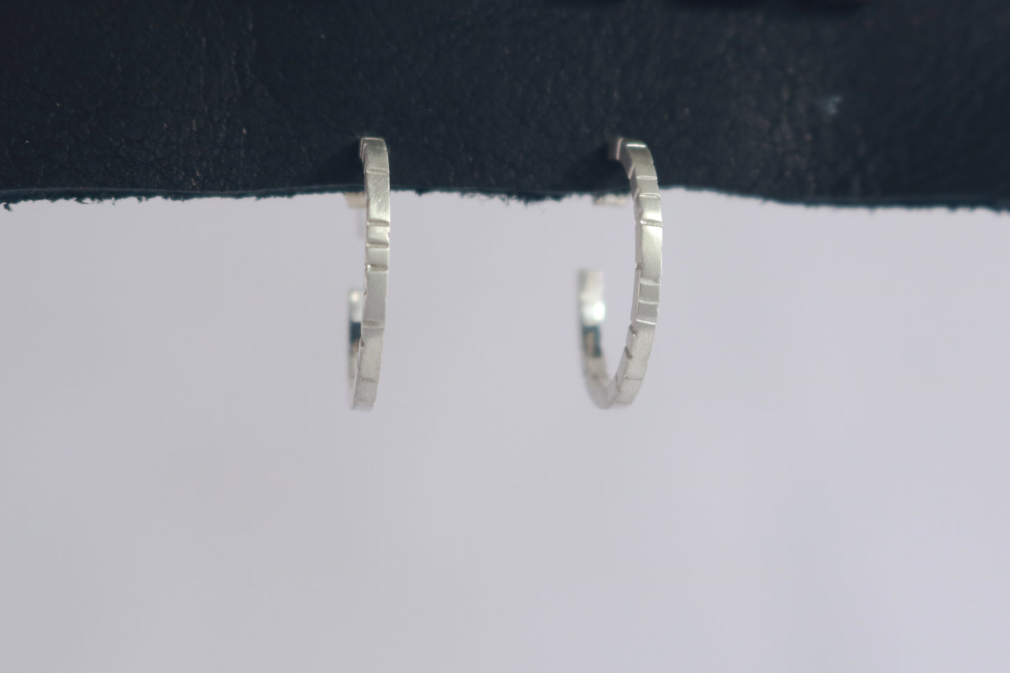 Thin sterling silver hoop earrings with randomly spaced black lines on each side.