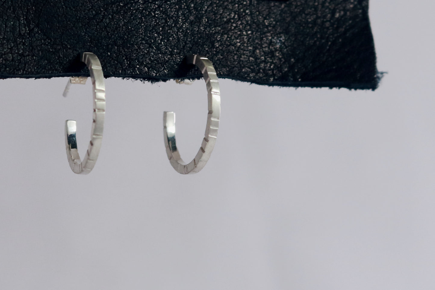 Thin sterling silver hoop earrings with randomly spaced black lines on each side.