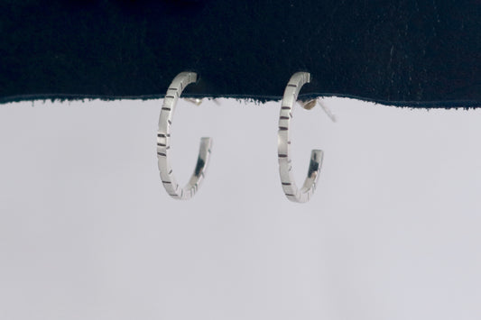 Thin sterling silver hoop earrings with randomly spaced black lines on each side.