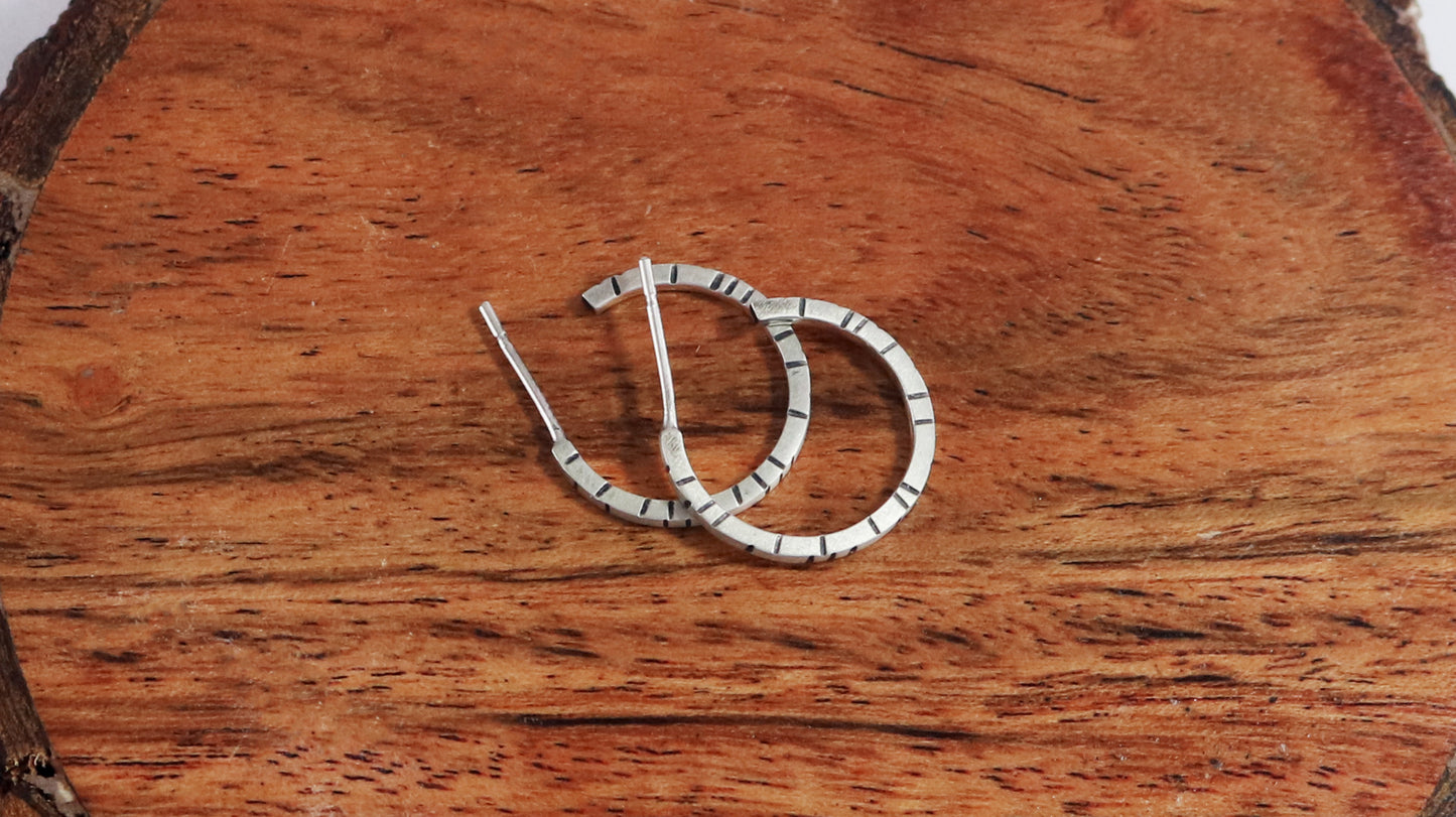 Thin sterling silver hoop earrings with randomly spaced black lines on each side.