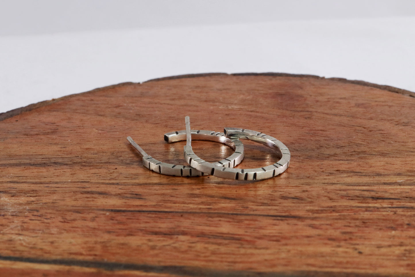 Thin sterling silver hoop earrings with randomly spaced black lines on each side.