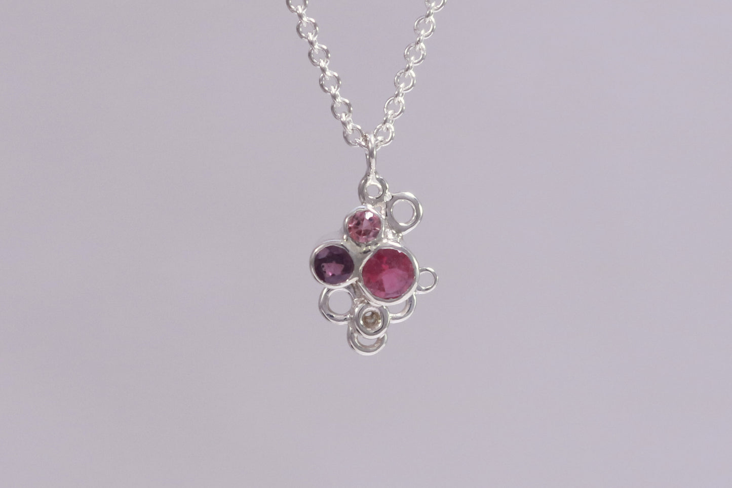 Three pink gemstones of descending sizes set in sterling silver bezels, grouped together in the shape of a triangle. Around the triangle are open silver circles. The pendant hangs on a sterling silver chain.