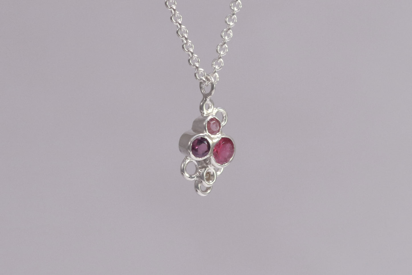 Three pink gemstones of descending sizes set in sterling silver bezels, grouped together in the shape of a triangle. Around the triangle are open silver circles. The pendant hangs on a sterling silver chain.