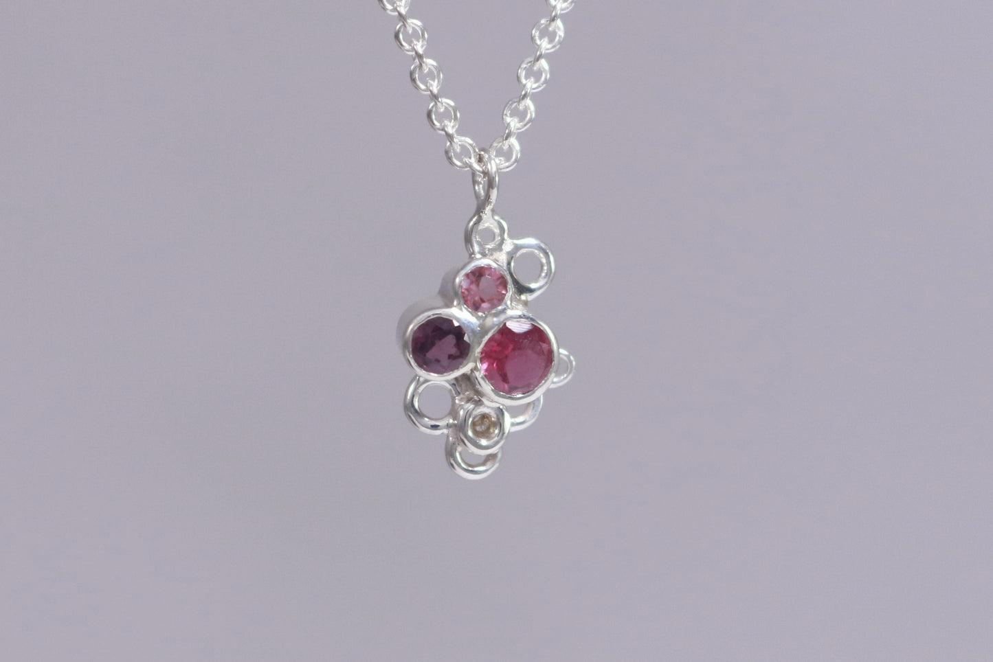 Three pink gemstones of descending sizes set in sterling silver bezels, grouped together in the shape of a triangle. Around the triangle are open silver circles. The pendant hangs on a sterling silver chain.