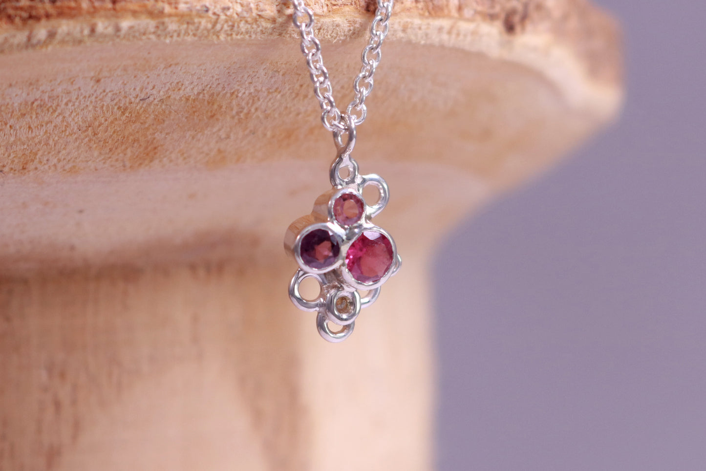 Three pink gemstones of descending sizes set in sterling silver bezels, grouped together in the shape of a triangle. Around the triangle are open silver circles. The pendant hangs on a sterling silver chain.