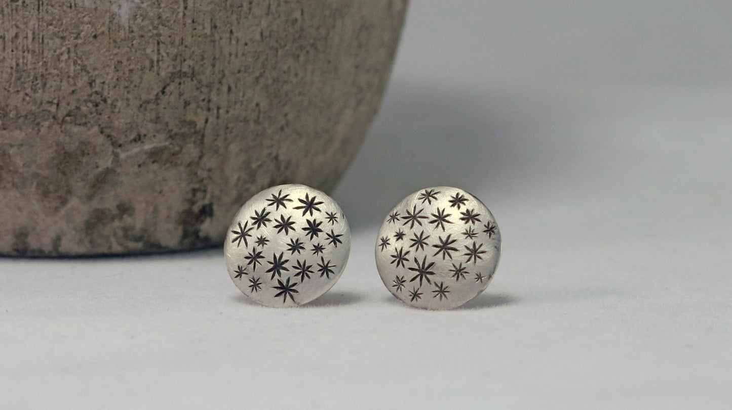 A pair of round, domed, silver, stud earrings with hand carved black stars.