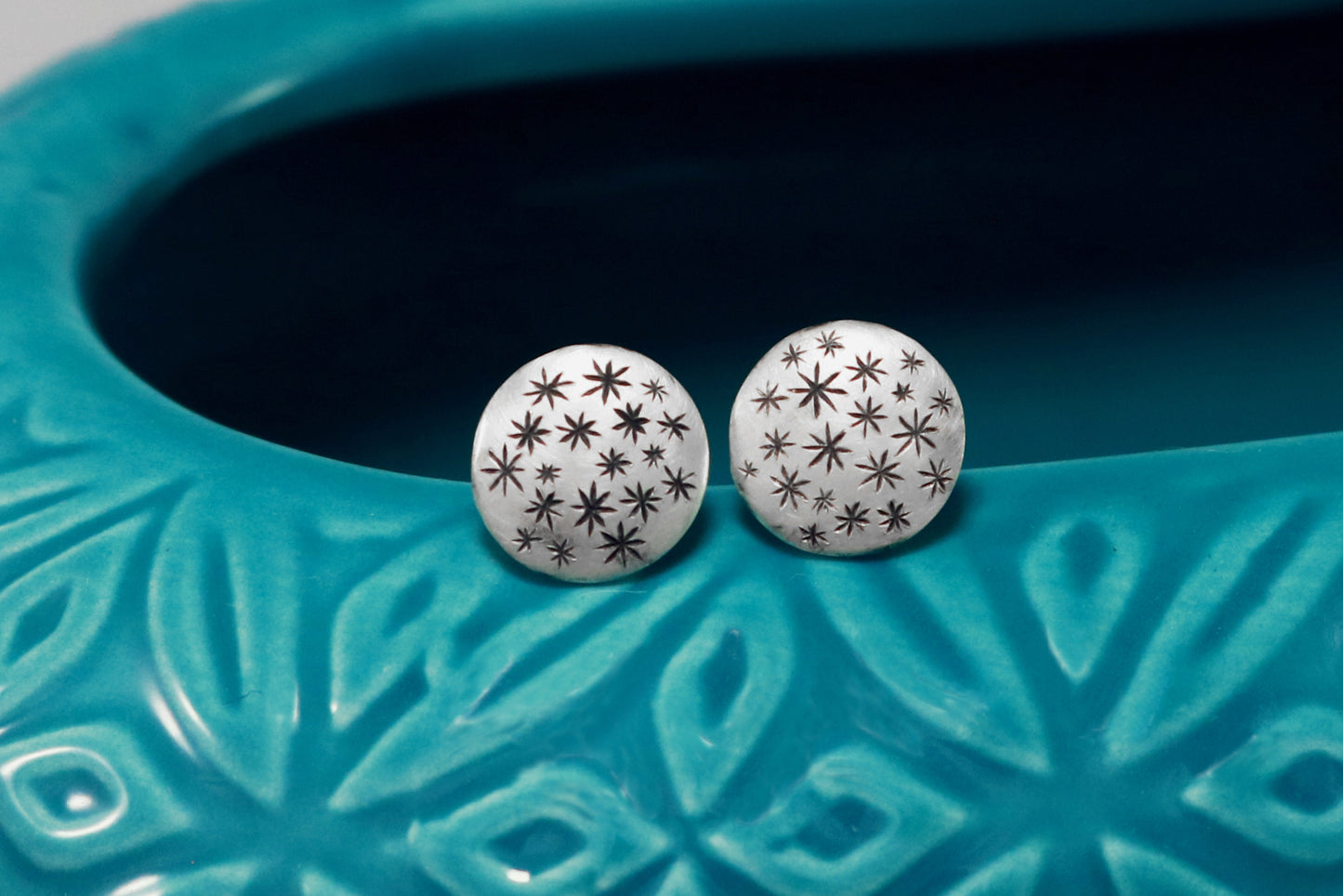 A pair of round, domed, silver, stud earrings with hand carved black stars.