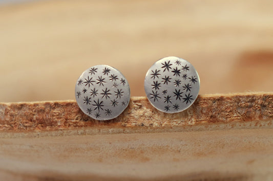 A pair of round, domed, silver, stud earrings with hand carved black stars.