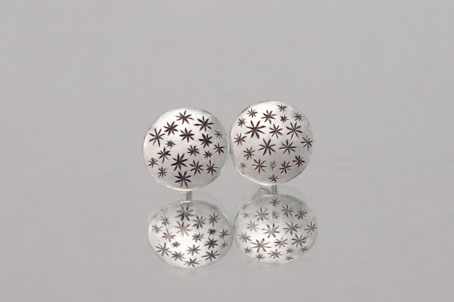 A pair of round, domed, silver, stud earrings with hand carved black stars.