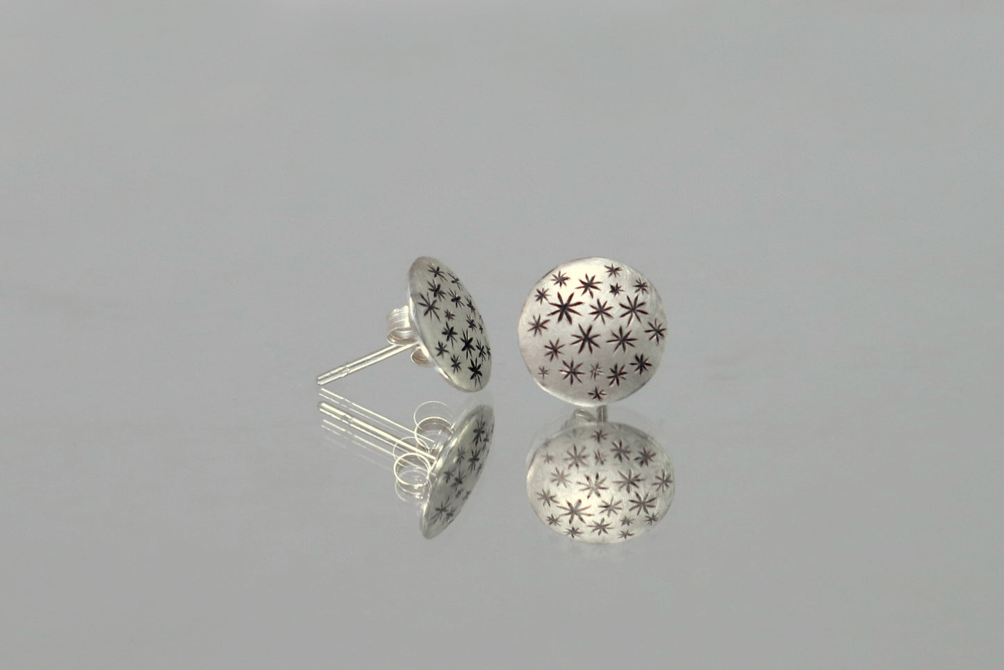 A pair of round, domed, silver, stud earrings with hand carved black stars.
