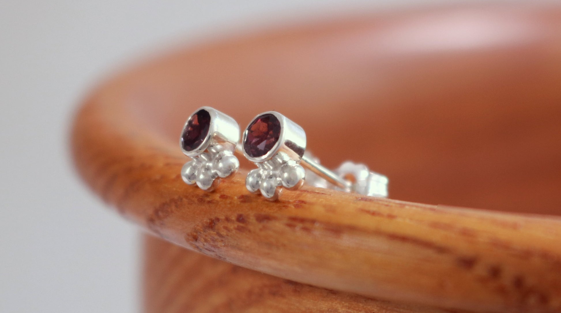 A pair of deep pink, round, faceted rhodolites set in sterling silver bezels with three silver bubbles aligned along the bezel.