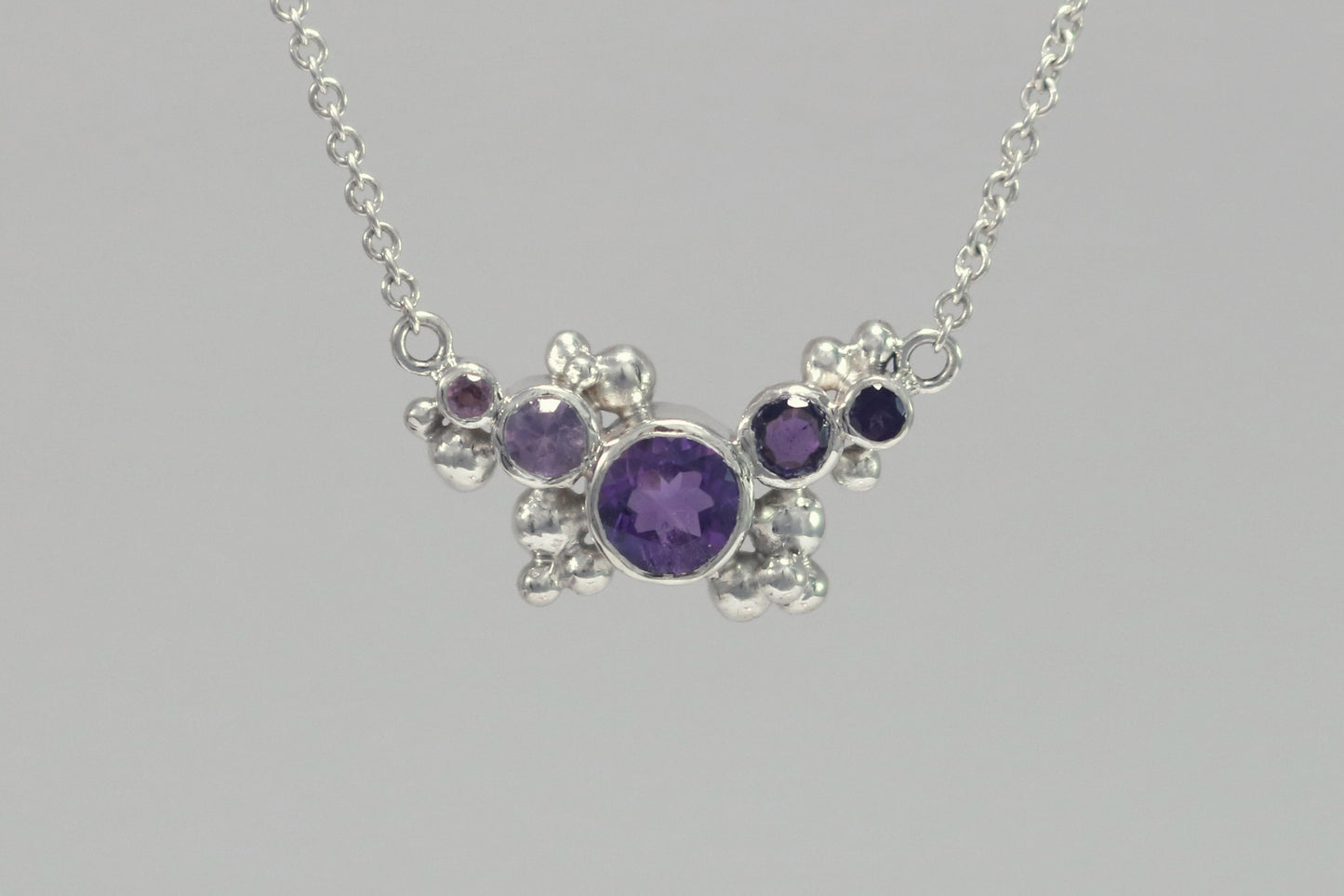 Different shades of round amethyst stones, surrounded by silver bubbles on a silver chain.
